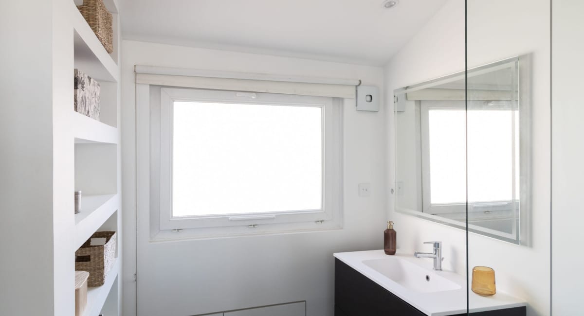 Salle de bain blanche avec deux fenêtres, un miroir et un lavabo.