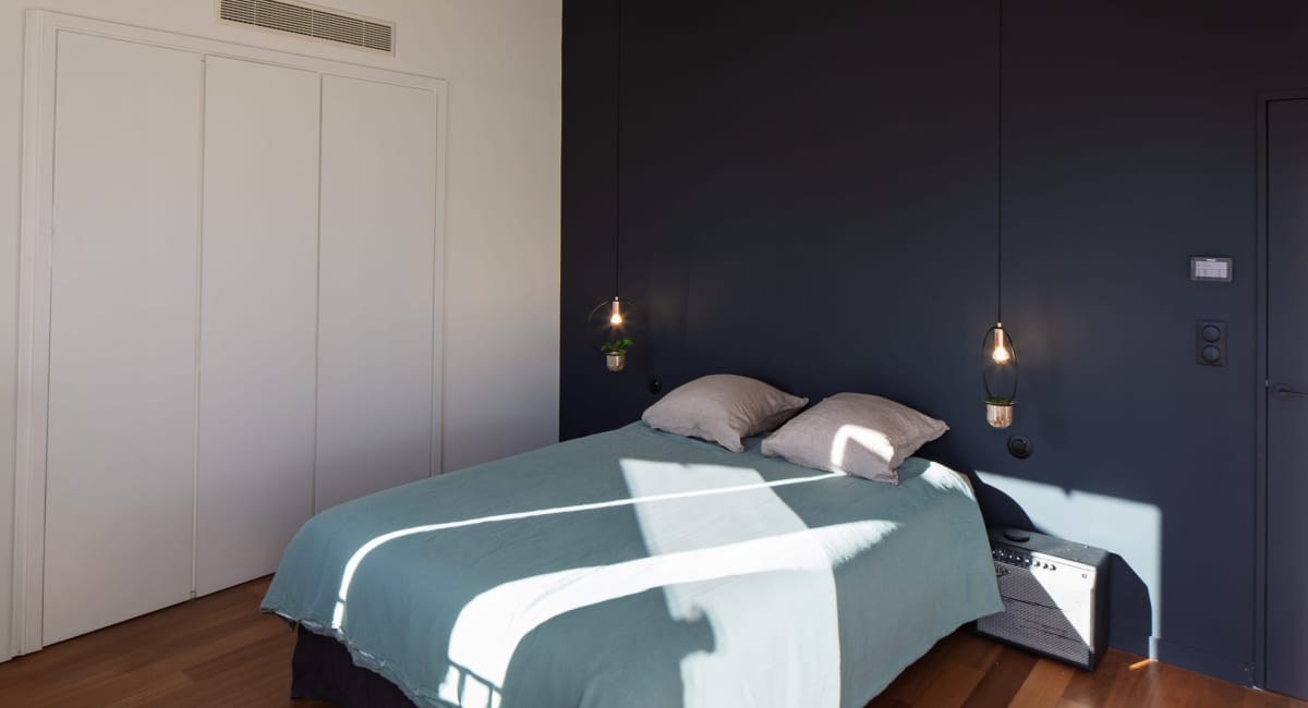 Chambre moderne avec un lit bleu, un mur bleu foncé et un éclairage suspendu.