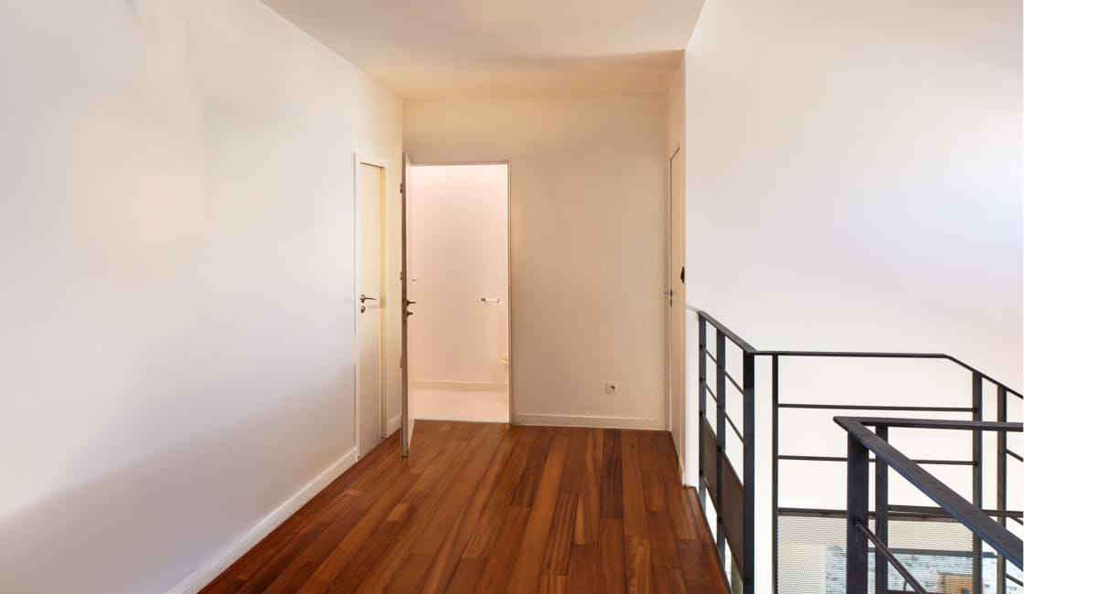Un couloir lumineux avec des murs blancs et un plancher en bois.
