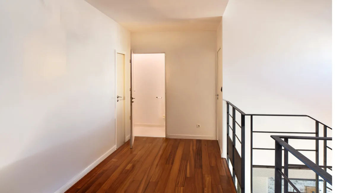 Un couloir lumineux avec des murs blancs et un plancher en bois.