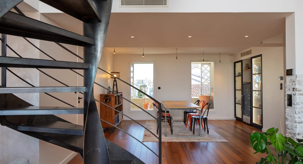 Intérieur d'un salon moderne avec une escalier en métal et une salle à manger lumineuse.