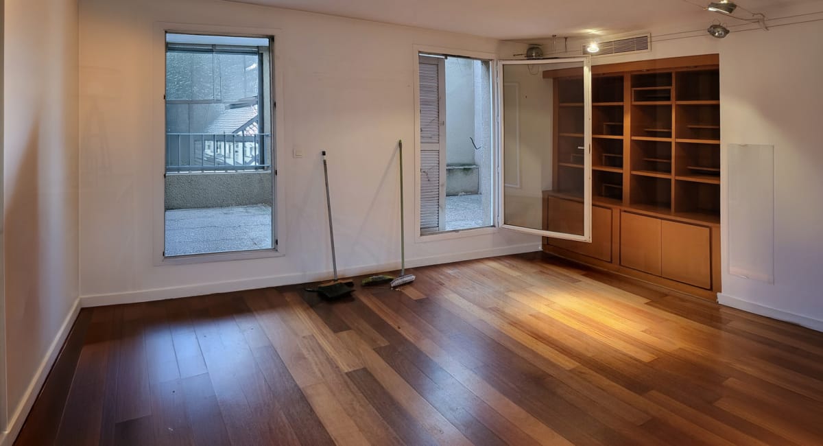 Pièce lumineuse avec parquet, fenêtre et bibliothèque ouverte, ambiance intérieure.