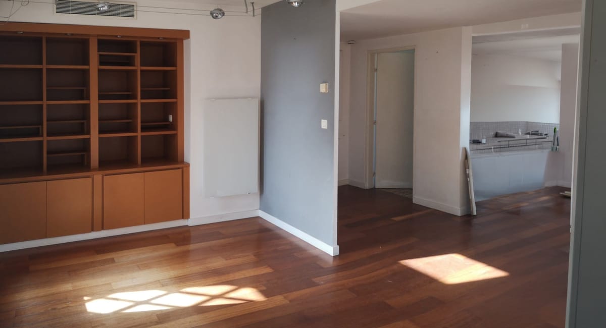 Intérieur d'un salon avec une bibliothèque en bois et vue sur une cuisine moderne.