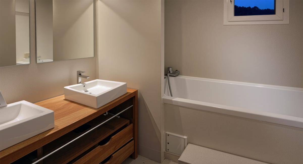 Salle de bain moderne avec lavabo, miroir et baignoire intégrée.