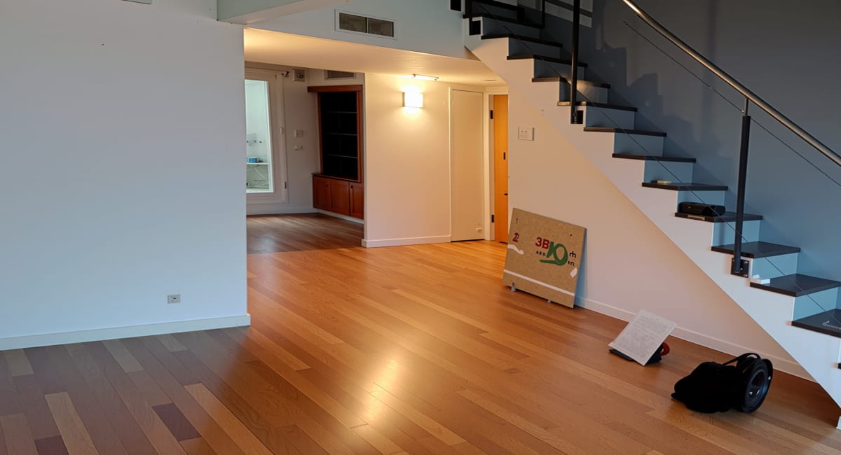 Intérieur d'un appartement avec escalier, plancher en bois et un panneau indiquant la superficie.