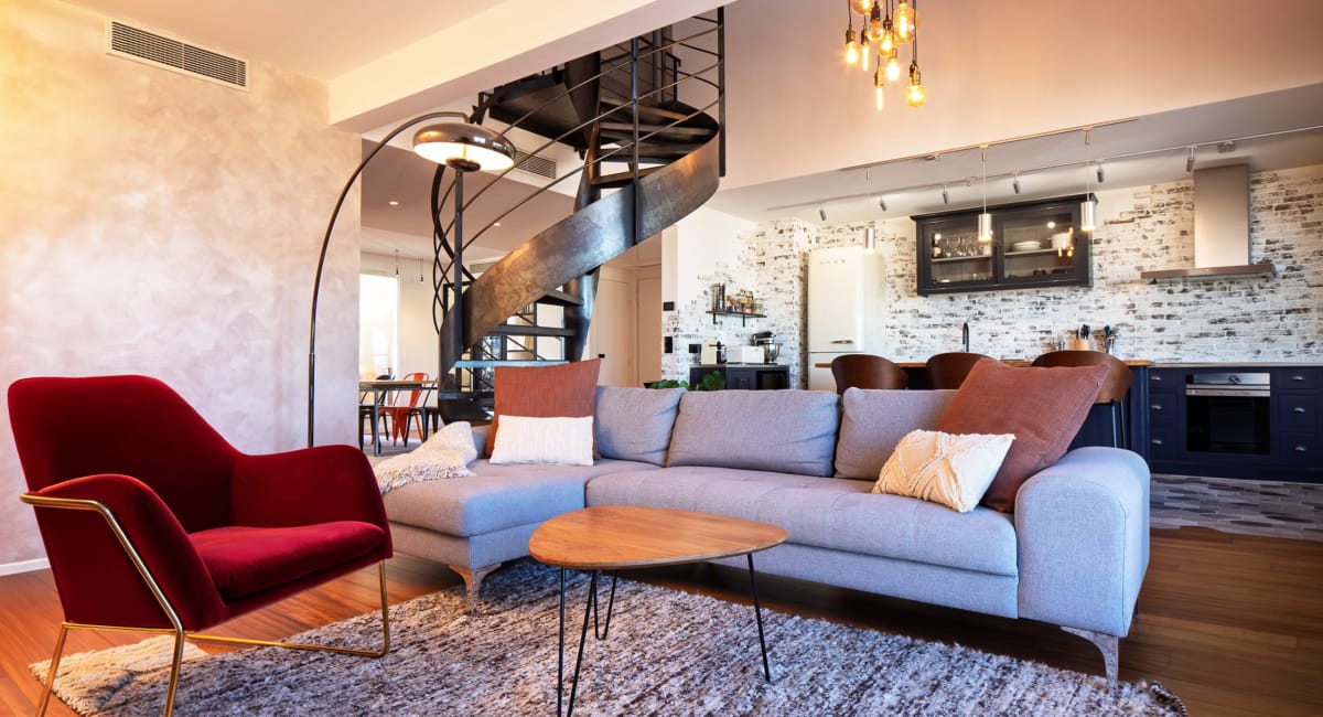 Intérieur moderne et chaleureux avec canapé gris, éclairage design et escalier en fer forgé.