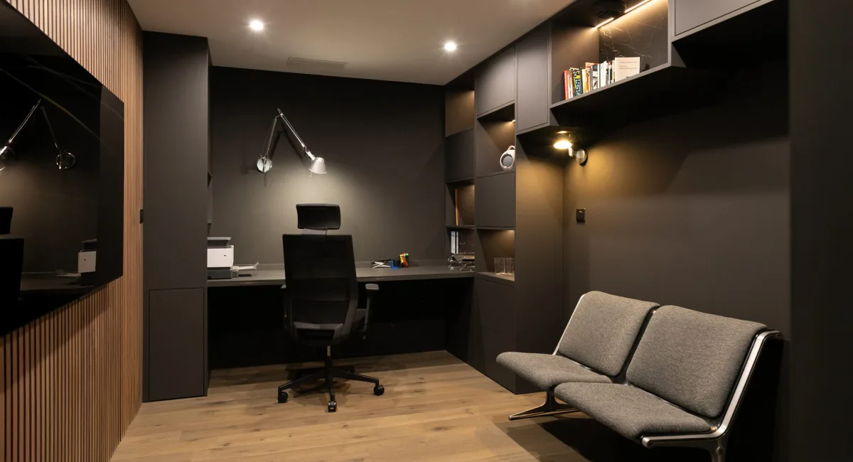 Bureau sombre et élégant avec un fauteuil et une petite banquette, ambiance moderne et chaleureuse.
