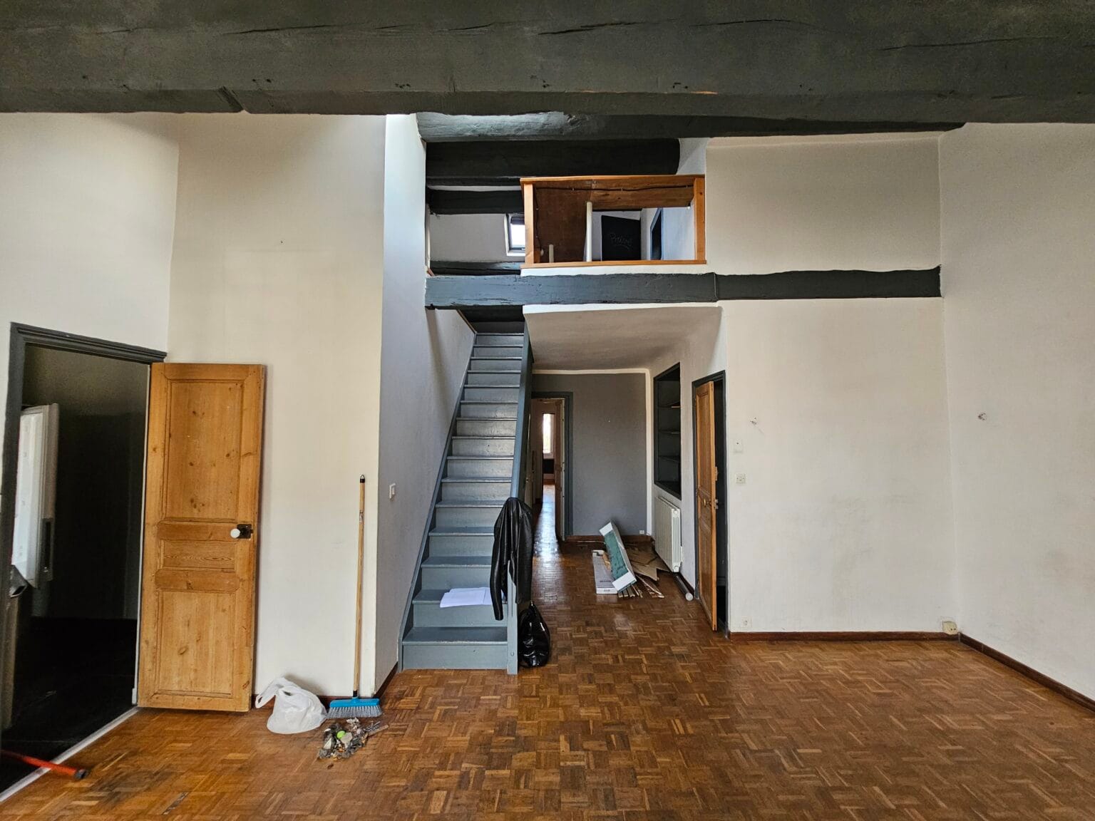 Intérieur d'un grand espace avec escalier, poutres apparentes et plancher en bois.