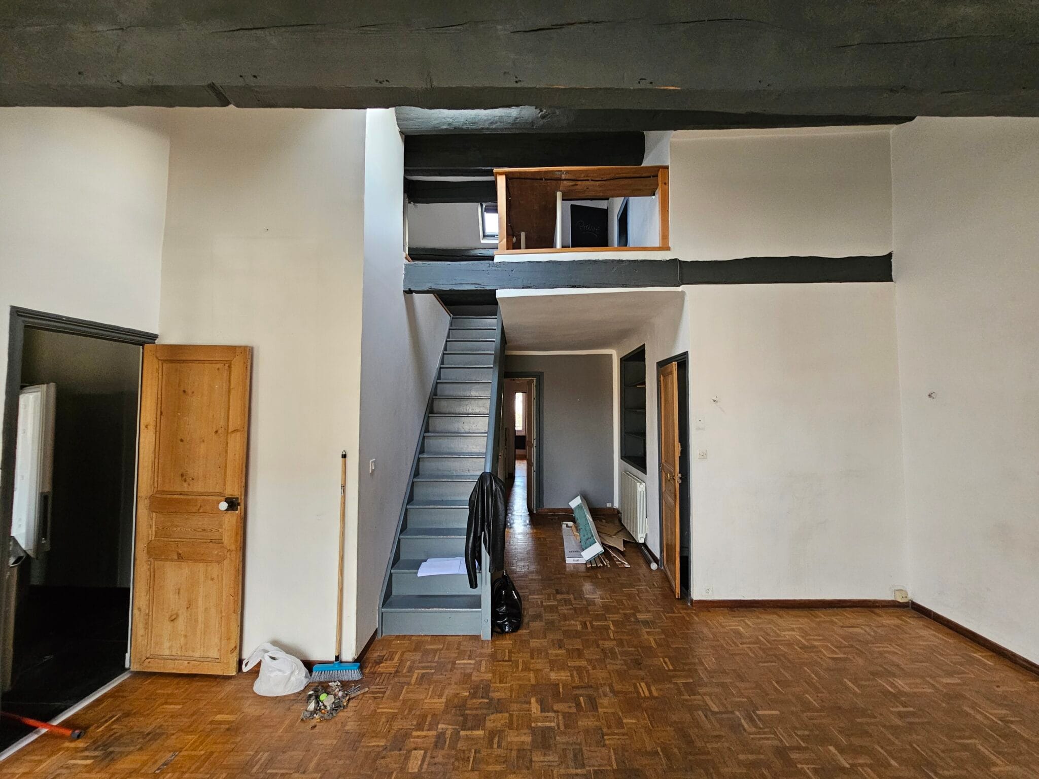 Intérieur d'un grand espace avec escalier, poutres apparentes et plancher en bois.