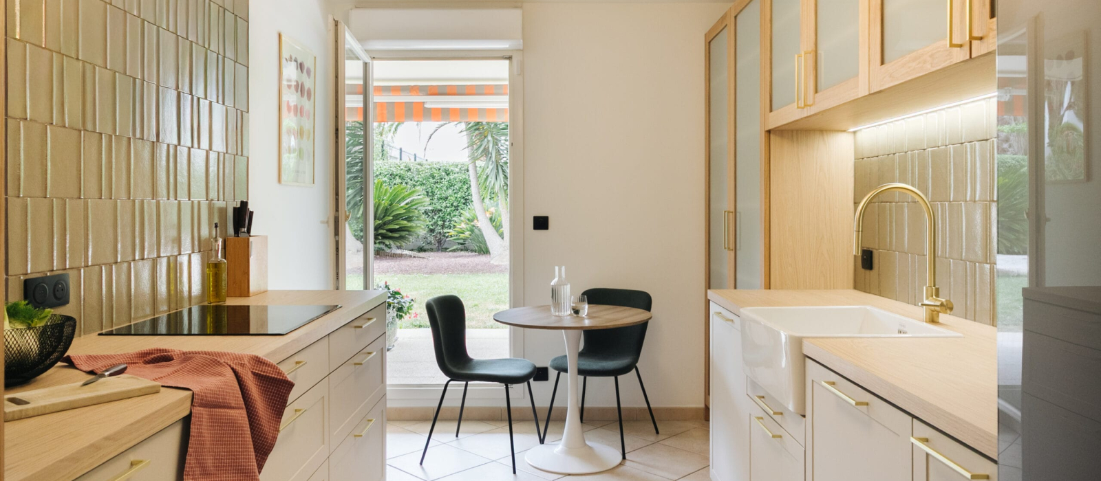 Cuisine moderne et lumineuse avec plan de travail en bois, meubles blancs et un petit coin repas près d'une porte-fenêtre.