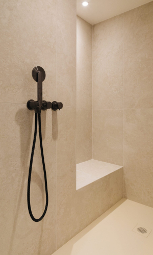 Douche moderne avec carrelage beige, équipée d'un pommeau noir et d'un banc intégré.