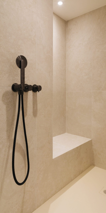 Douche moderne avec carrelage beige, équipée d'un pommeau noir et d'un banc intégré.