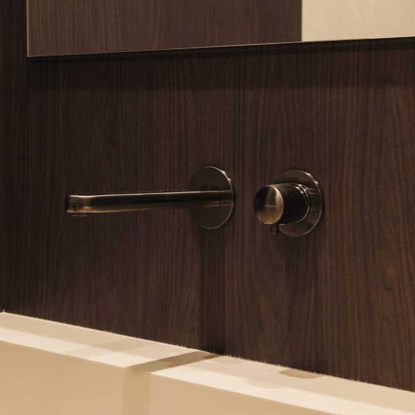 Robinetterie encastrée noire mate installée sur un mur en bois sombre au-dessus d'un lavabo blanc.