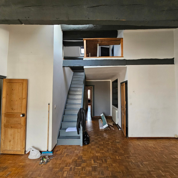 Intérieur d'un grand espace avec escalier, poutres apparentes et plancher en bois.